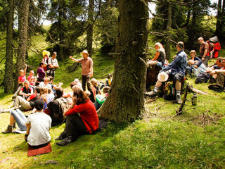 Mann erklärt einer Gruppe etwas im Wald beim Spirit am Berg im Mountain Resort Feuerberg