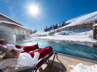 Paar entspannt im Winter in der Sonne am Pool der Alpentherme im Wellnesshotel in Kärnten